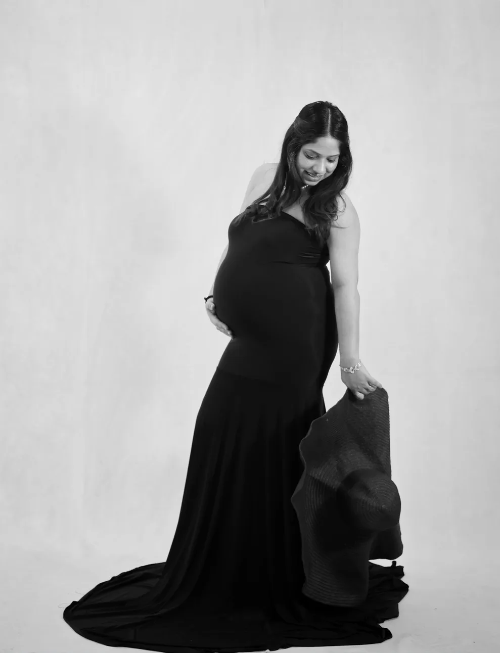 Black and white profile portrait of expectant mother sitting in a black dress