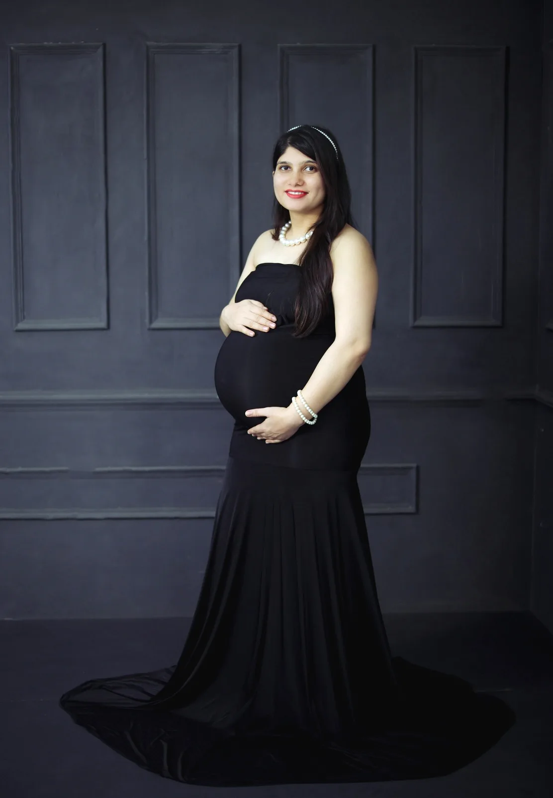 Expecting mother in an elegant black gown with hands resting on her baby bump