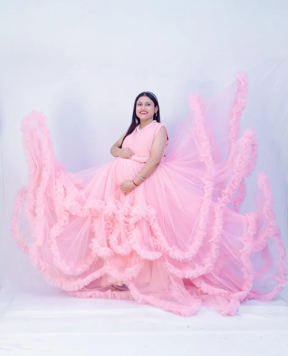 Expecting mother in a soft pink dress looking down lovingly at her baby bump