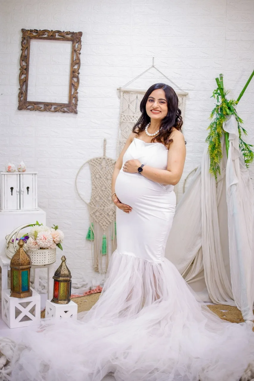 Expecting mother in a flowing white maternity gown during a studio portrait