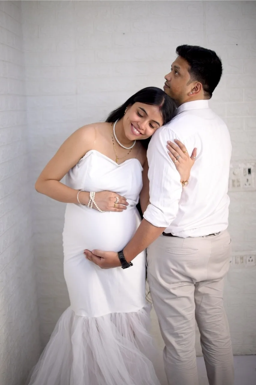 Expectant mother sitting in a white gown against a soft studio backdrop