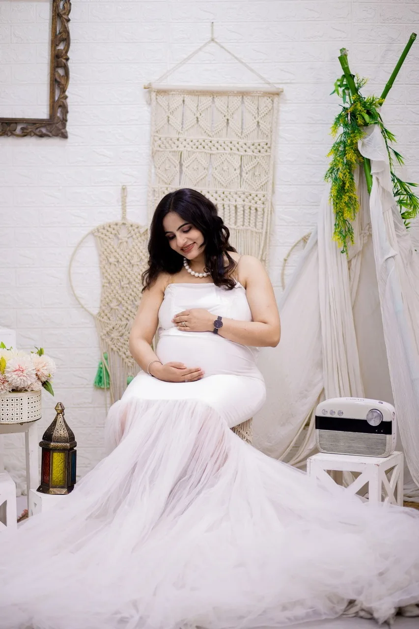 Expecting mother standing in a white dress under a decorative floral wreath