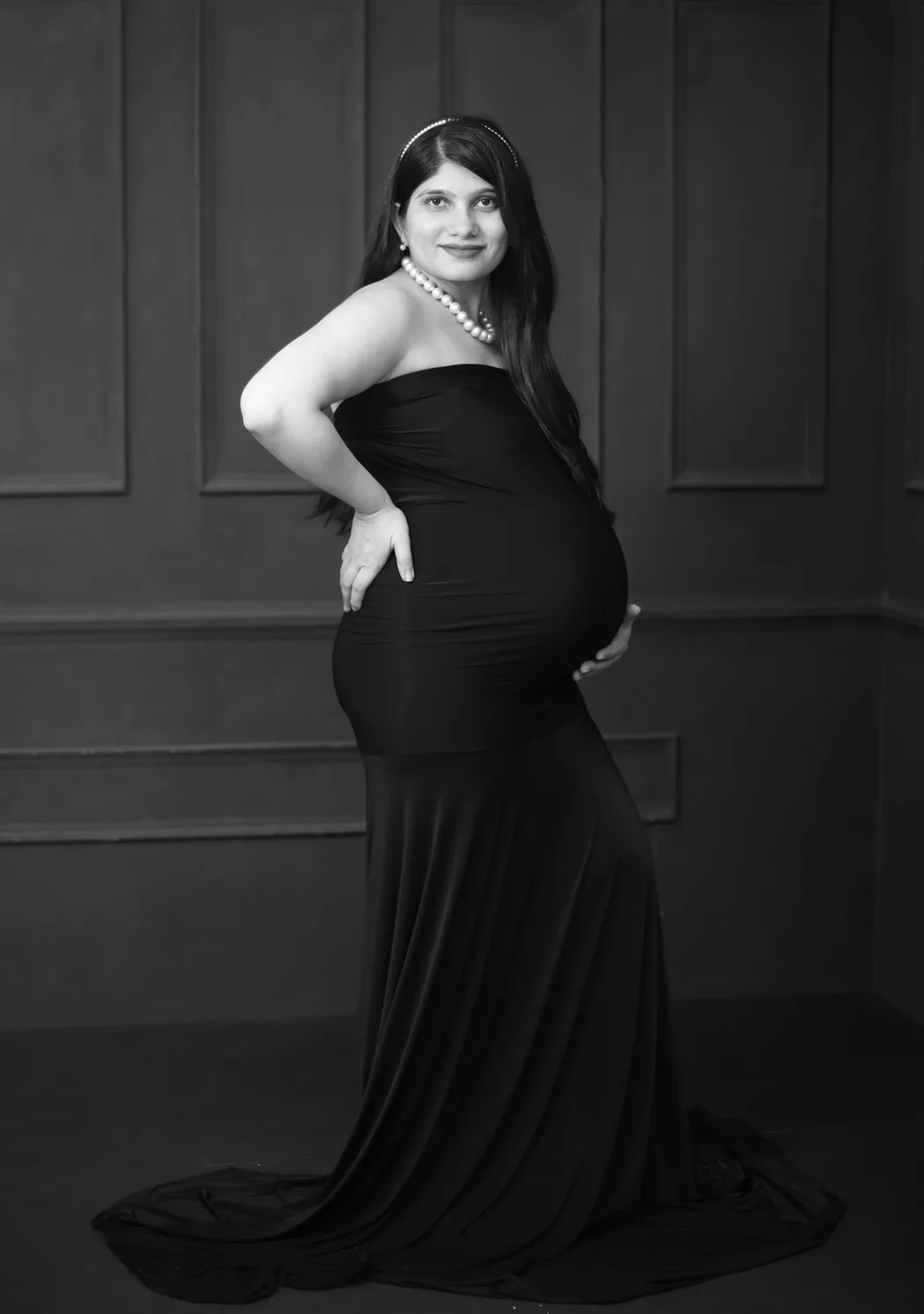 Expecting mother in a black gown looking over her shoulder with hand on her back