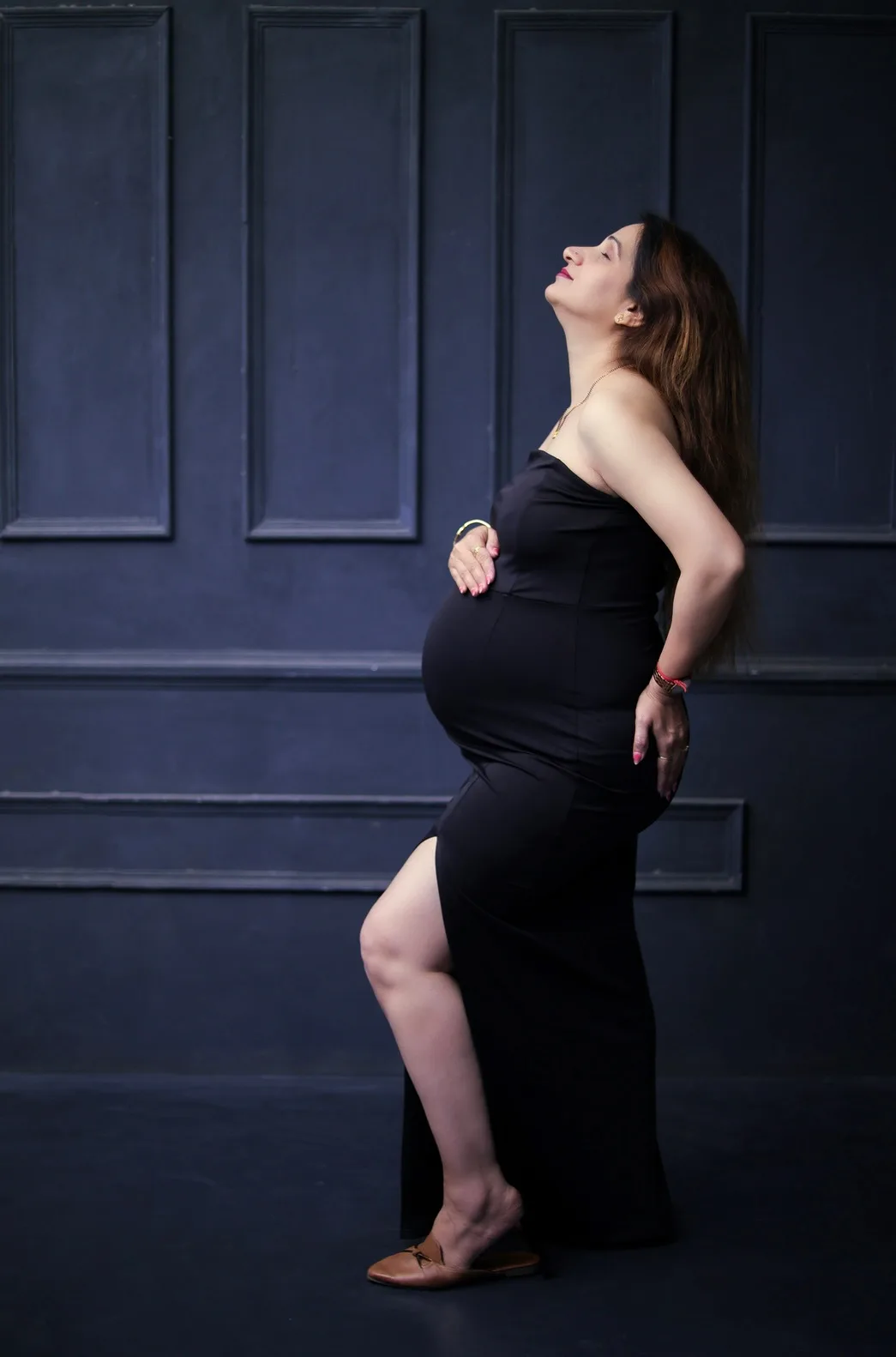 Expecting mother in a black gown with hand on her baby bump looking upward