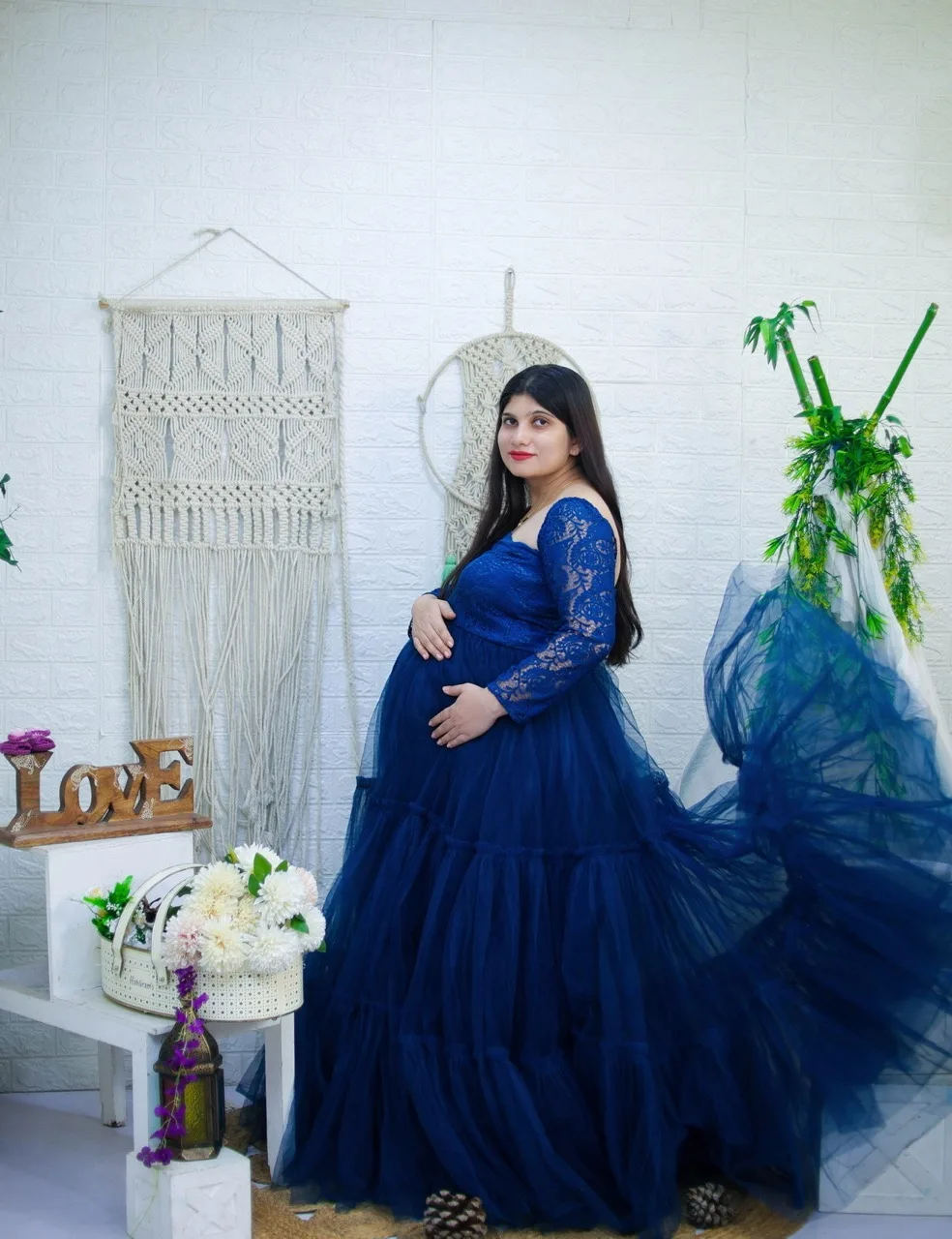Expecting mother in a blue bohemian dress posing against a rustic backdrop