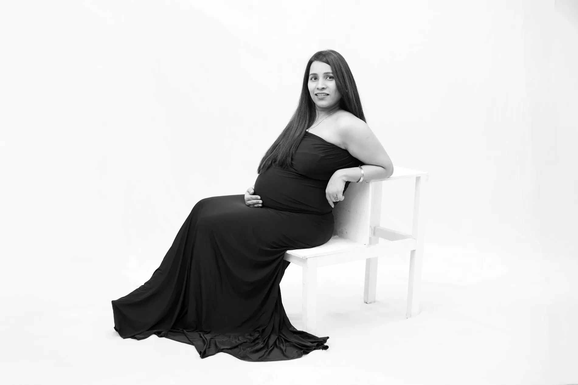 Classic black and white studio portrait of expectant mother in a fitted black gown