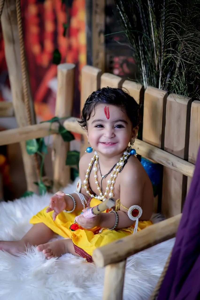 Happy baby boy in Krishna costume smiling on a white fur jhula, Janmashtami Krishna theme baby photoshoot in Delhi NCR.