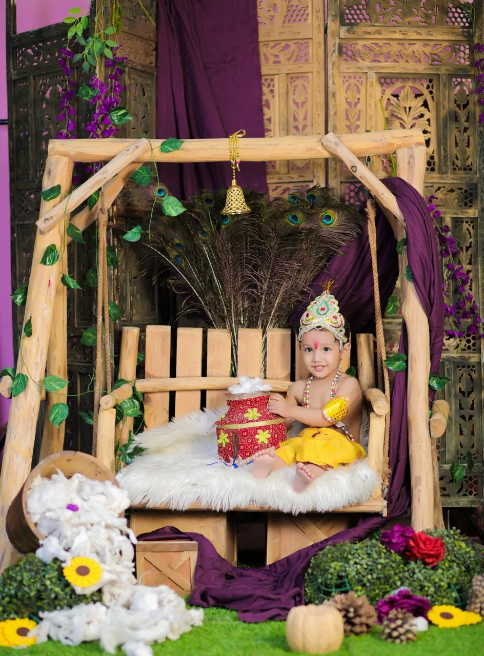 Cute baby Krishna holding a butter pot on a decorated studio jhula, Janmashtami Krishna theme baby photoshoot in Delhi NCR.