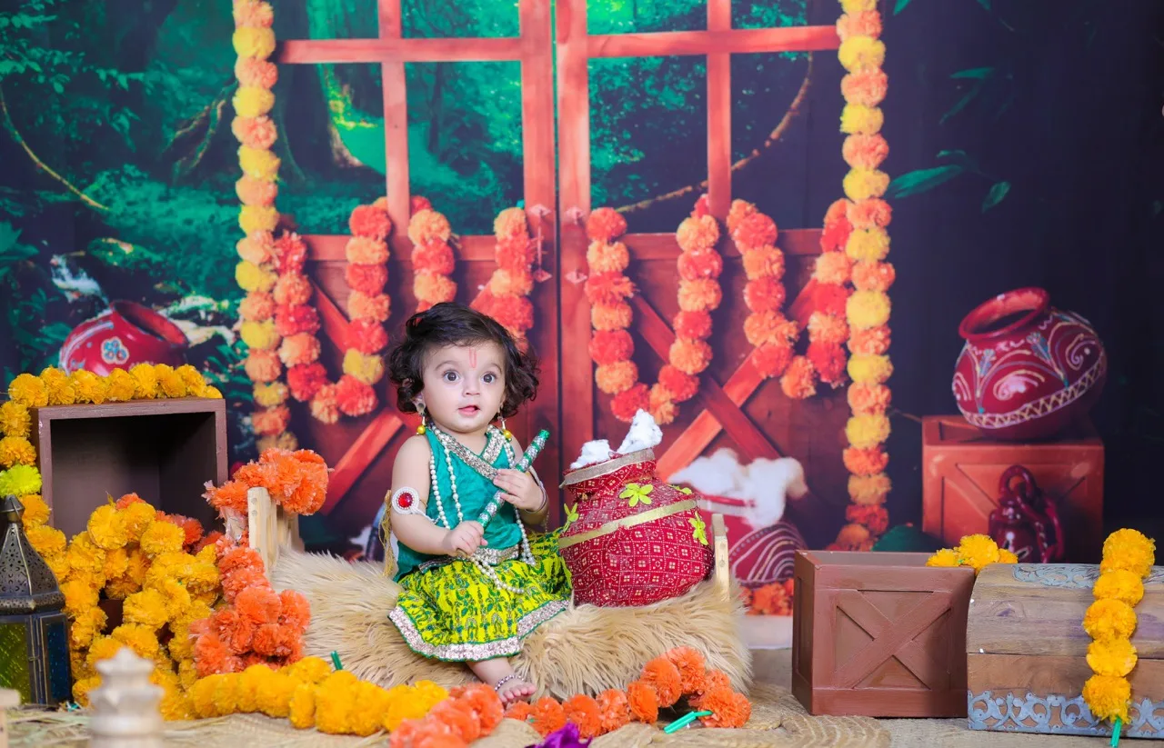 A baby in a green Radha dress holds a butter pot in a Vrindavan theme, Janmashtami Krishna theme baby photoshoot in Delhi NCR.